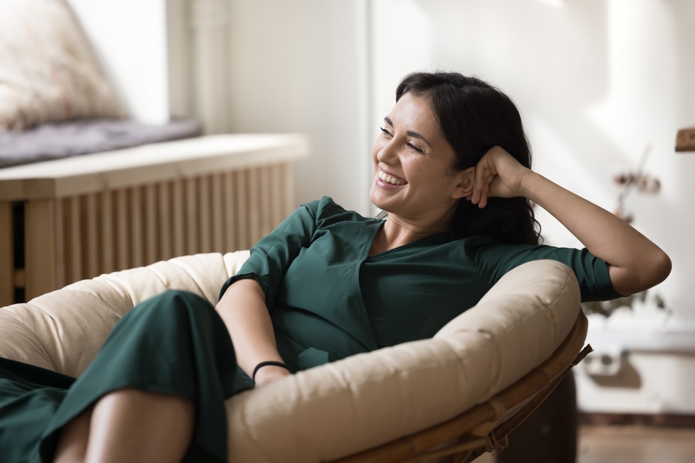 A smiling woman in a green dress relaxing in a cushioned chair