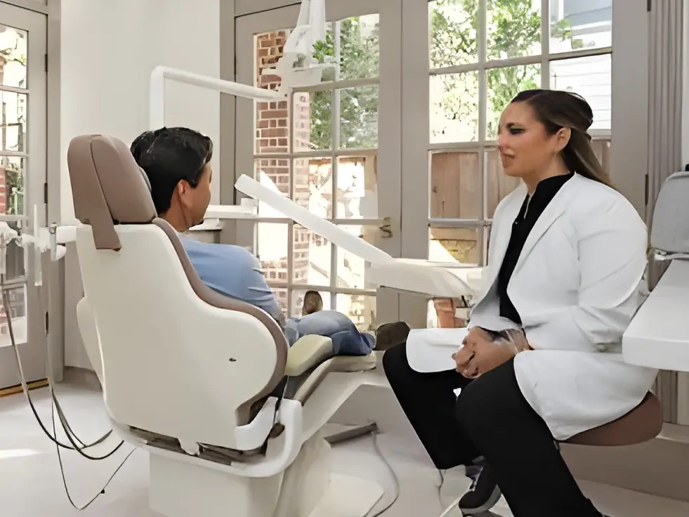 A dentist speaking with a patient in a bright treatment room