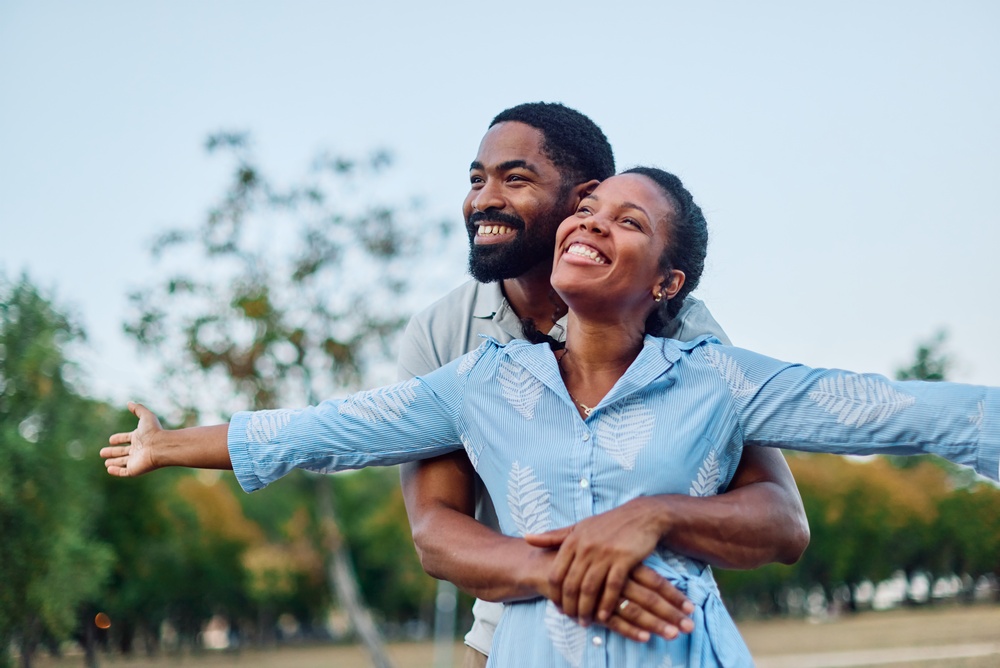 A smiling couple embracing outdoors with the woman stretching out her arms
