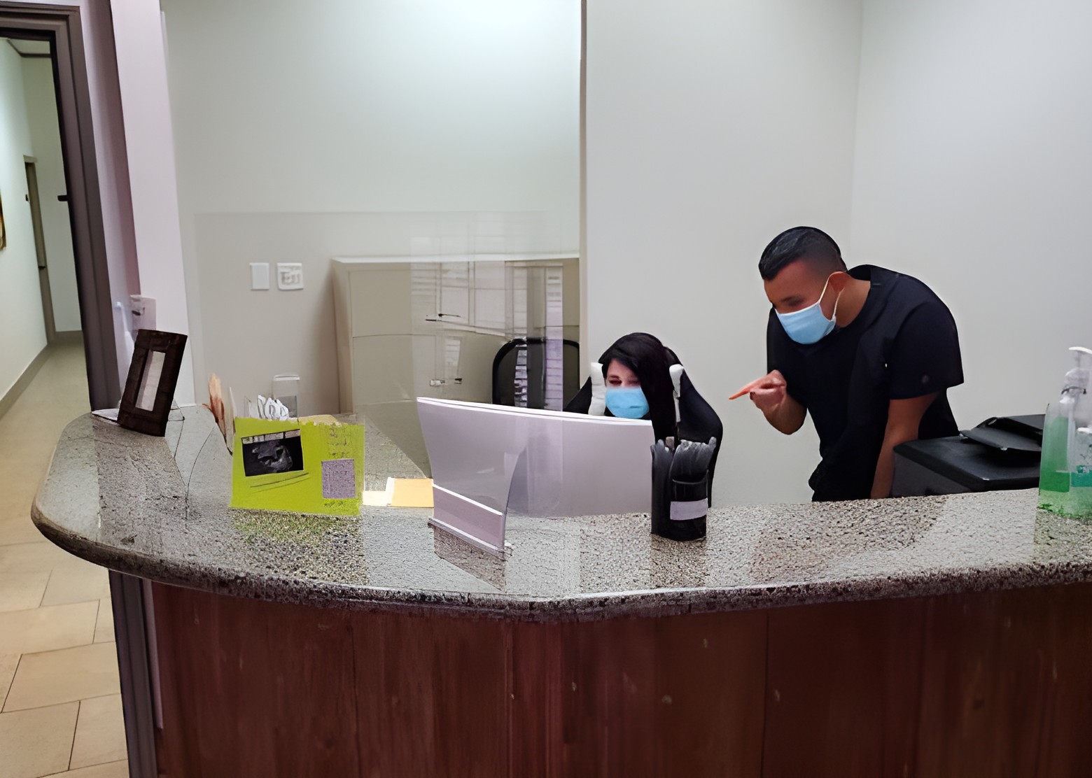 Two team members wearing masks and working together at the dental office reception desk