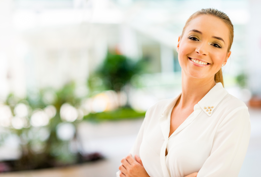 A smiling woman in a white blouse with her arms folded