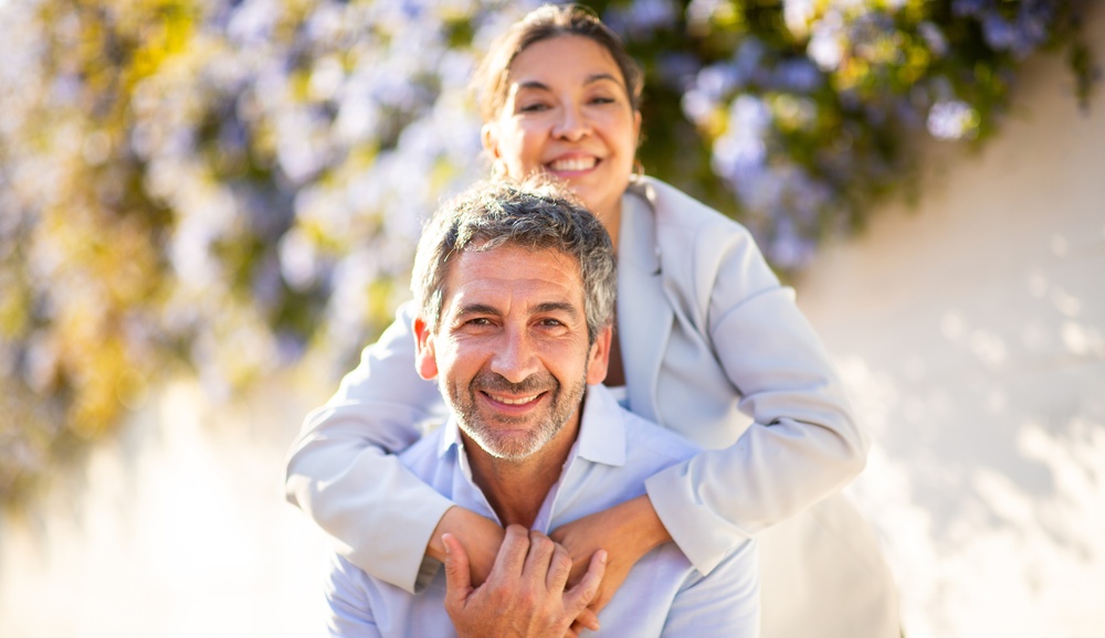 A smiling man carrying a smiling woman on his back outdoors