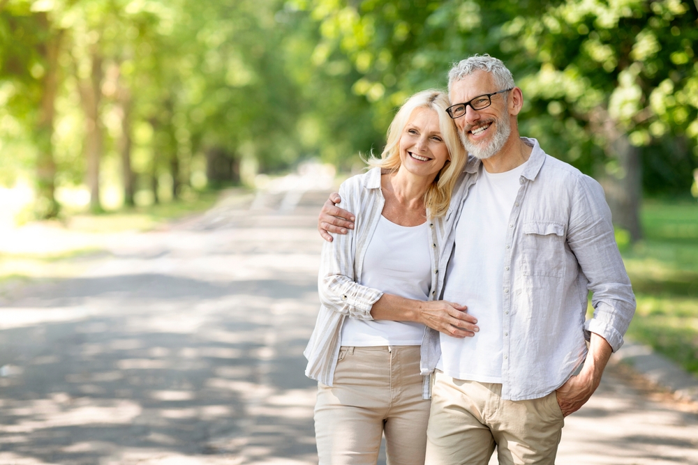 A smiling older couple embracing on a tree-lined path
