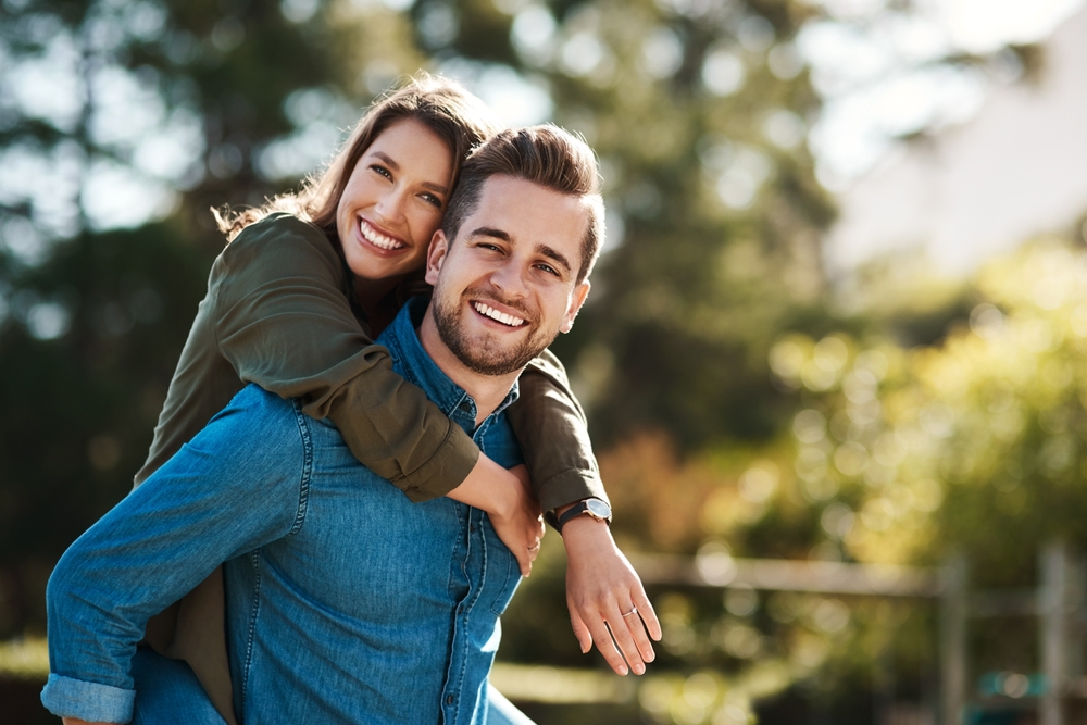 A smiling man giving a woman a piggyback ride outdoors