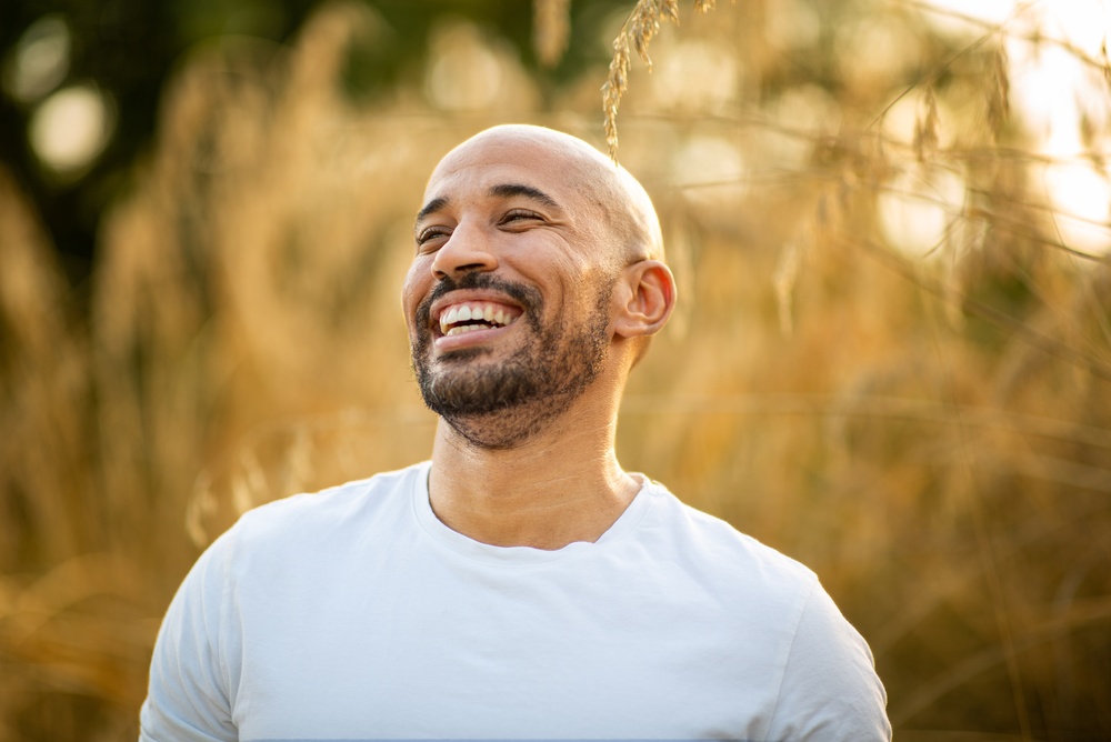 A smiling man in a white shirt outdoors in warm sunlight