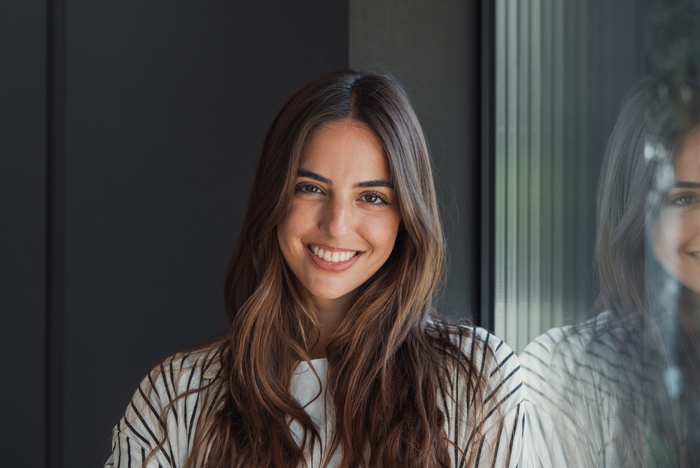 A smiling woman beside a window with her reflection in the glass