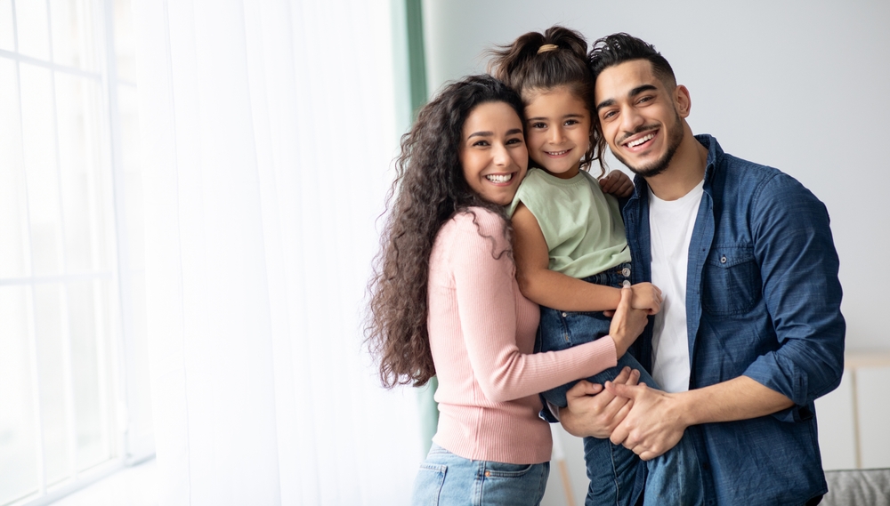 Smiling parents holding their daughter together at home