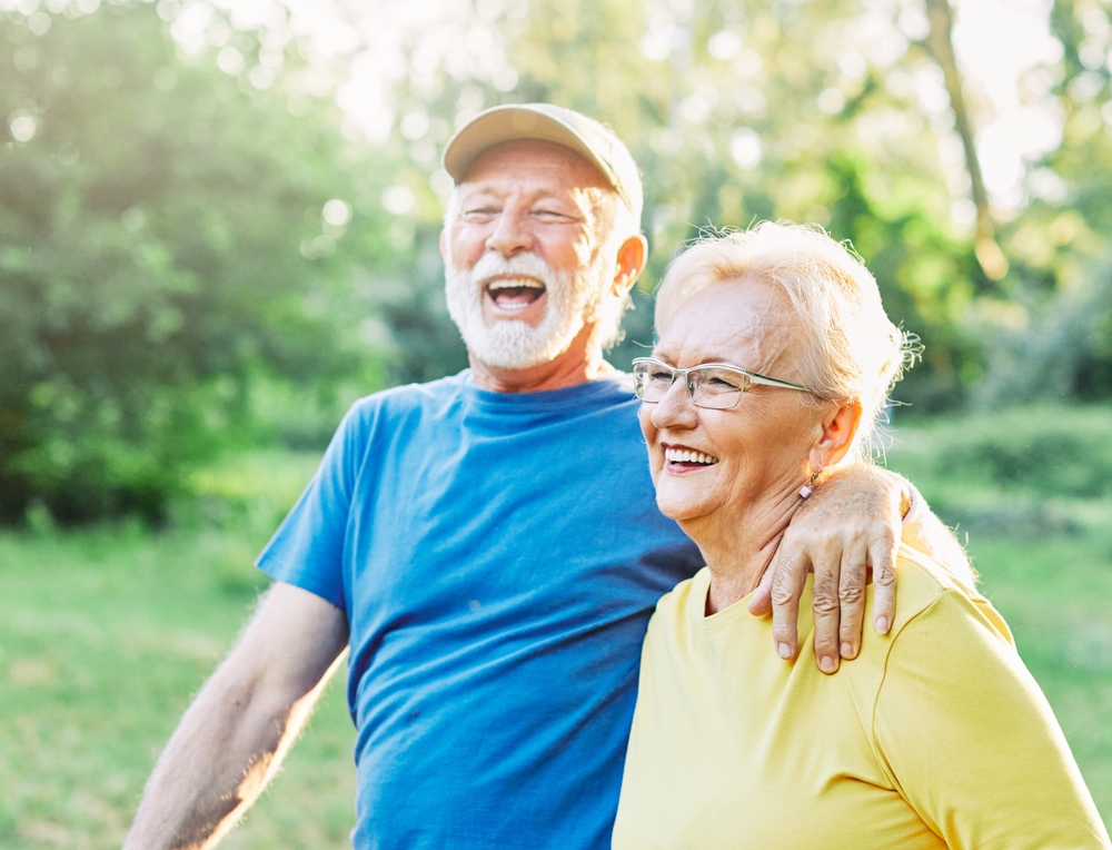 An older couple laughing outdoors with the man resting his arm around the woman