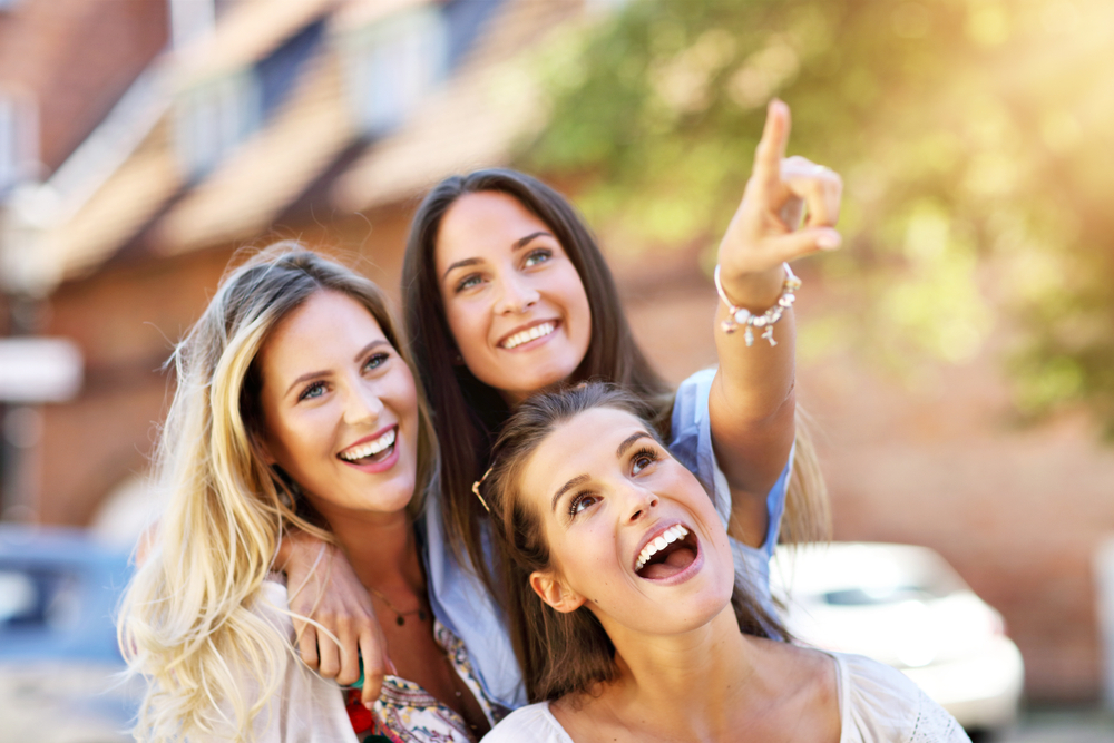 Three smiling women together outdoors, looking upward