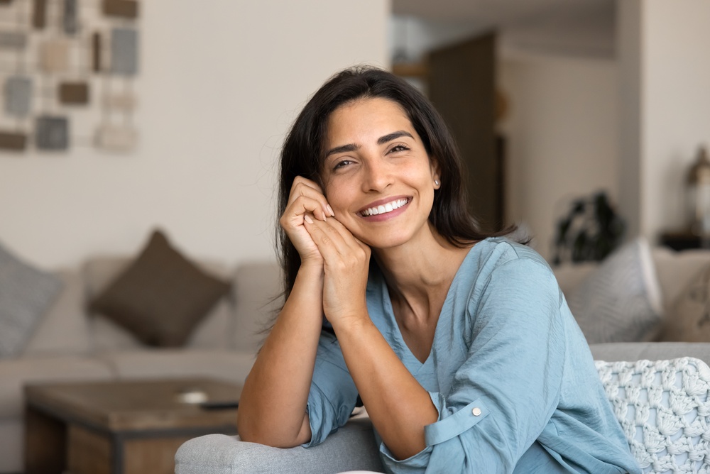 A smiling woman in a blue blouse seated at home