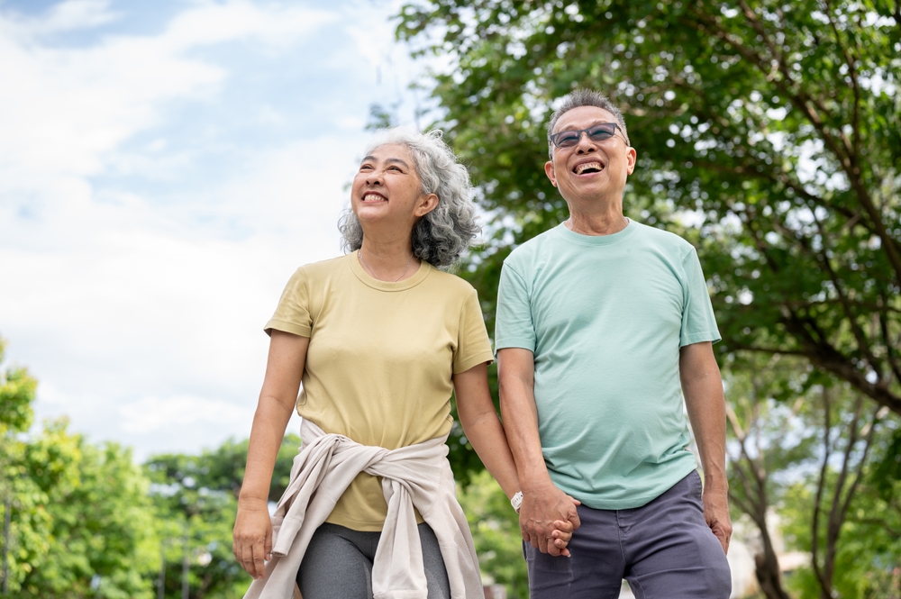 An older couple smiling and holding hands while walking outdoors