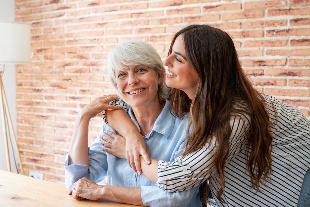 A younger woman embracing a smiling older woman seated at a table